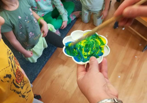 Dzieci obserwują powstawanie koloru zielonego – nauczycielka miesza farbę żółtą z niebieską.
